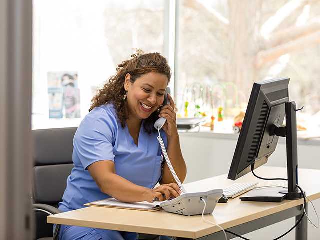 female health care worker sitting at computer while talking to a patient on the phone